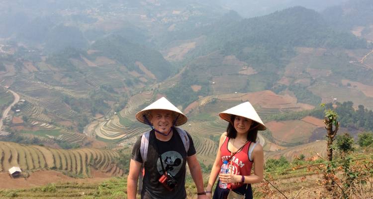 Zwei Touristen mit konischen Hüten vor terrassierten Feldern.