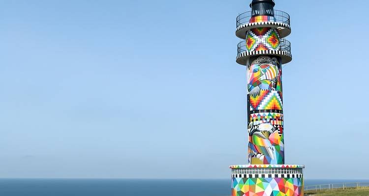 Kleurrijke vuurtoren tegen een blauwe lucht en oceaan.