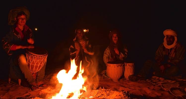 Groep mensen die 's nachts rond een kampvuur zitten in een woestijnomgeving.