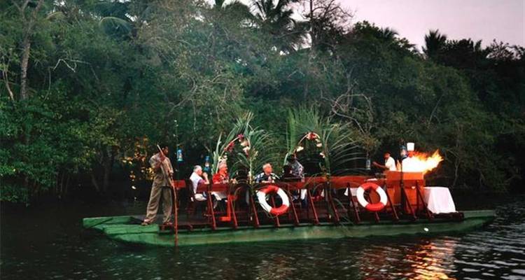 Groep mensen die dineren op een vlot op een rivier bij zonsondergang.