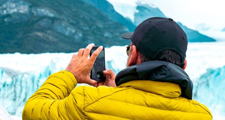 Hombre tomando una foto con un teléfono inteligente, con vista a un glaciar de fondo.