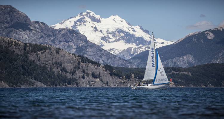 Boot zeilend op een meer met besneeuwde bergen.