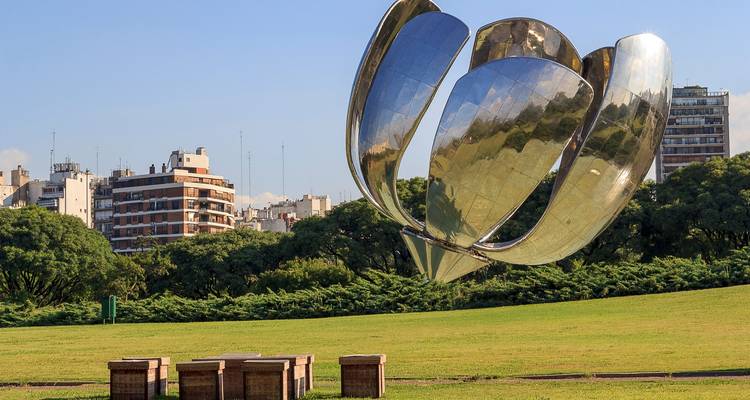 Metal flower sculpture in a public park with a city backdrop.