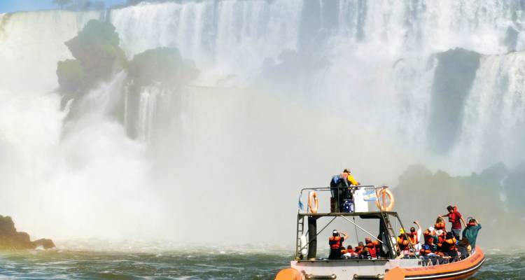 A group of people on a boat approaching large waterfalls.