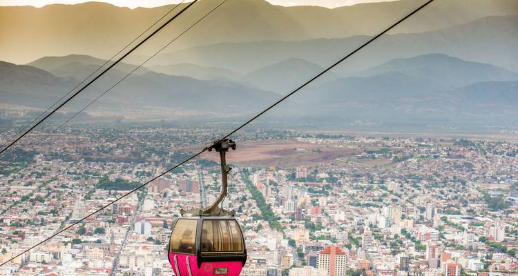 A cable car with a cityscape and mountain backdrop.