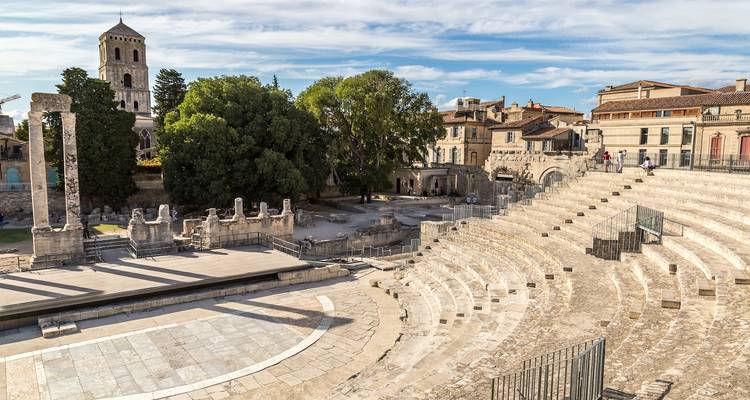Théâtre romain antique avec des sièges et des bâtiments anciens à proximité.