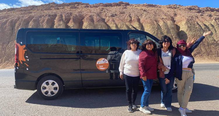 Grupo de turistas posando frente a una camioneta de turismo en un paisaje desértico.