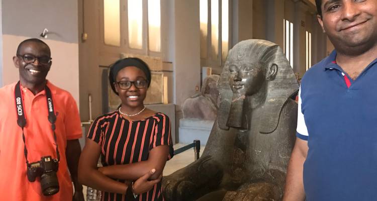 Groep mensen die poseren naast een farao standbeeld in een museum.
