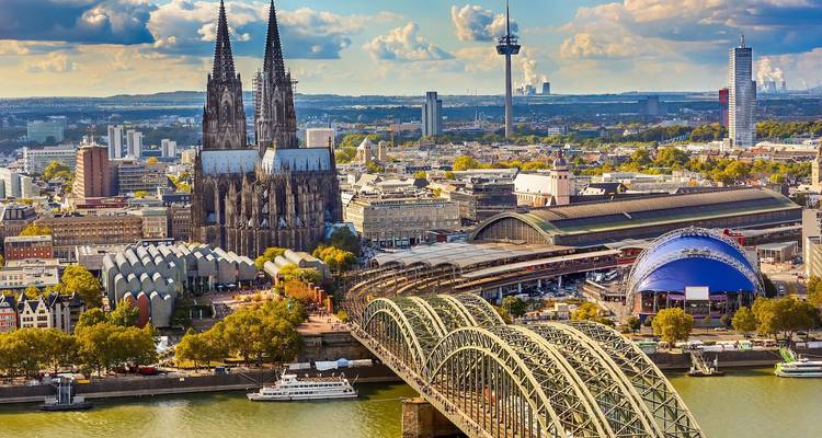 Iconic Cologne Cathedral towers above the Hohenzollern Bridge and Rhine River in golden light.