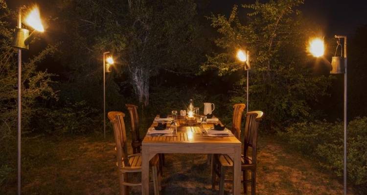 Outdoor-Dining-Bereich mit Fackeln, umgeben von Grünpflanzen.