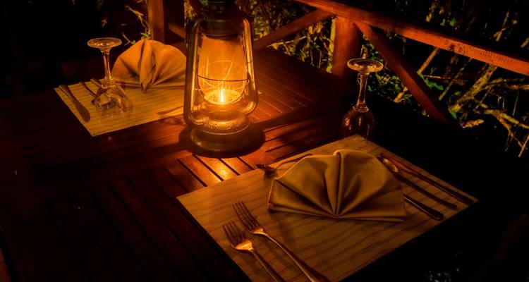 Intimate lantern-lit dining table set for two on a wooden deck after dark.