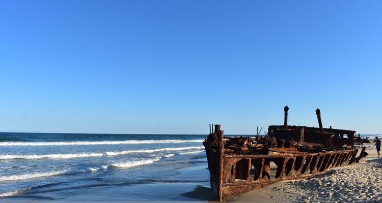 Épave rustique sur une plage de sable avec des vagues océaniques.