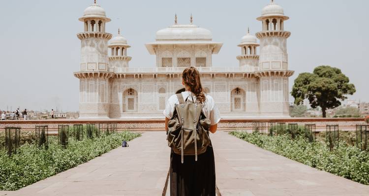 Individual facing a historic mausoleum with a backpack.
