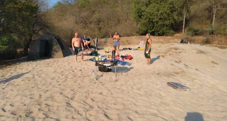Menschen stehen auf einem sandigen Strand mit sichtbarer Campingausrüstung.