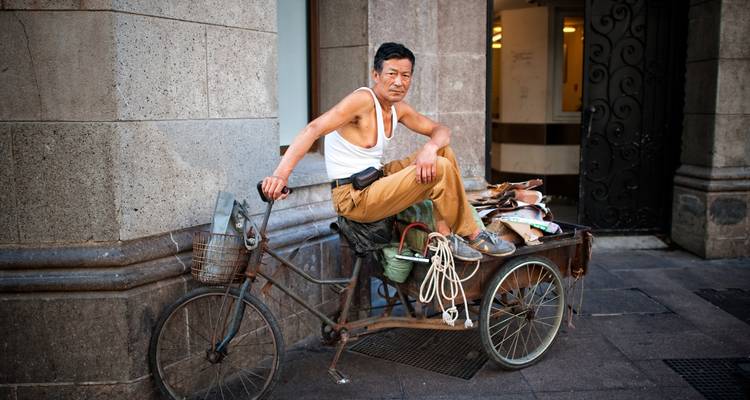 Homme assis sur un tricycle à charrette en milieu urbain.