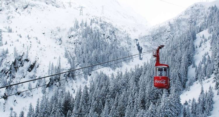 Red cable car traveling through a snowy forested mountain area.
