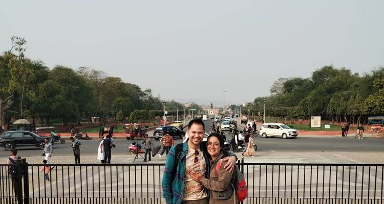 Deux voyageurs sourirent pour une photo à un point de vue de ville animée avec du trafic et des jardins derrière eux.