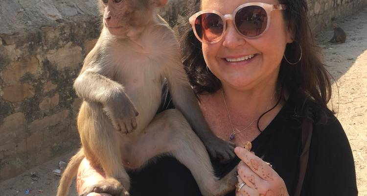 Une femme portant des lunettes de soleil sourit en tenant un petit singe sur son bras.
