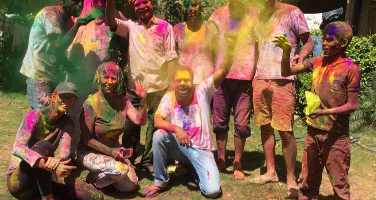 Un groupe joyeux couvert de poudres éclatantes célèbre Holi dans une cour herbeuse.