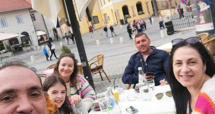 Famille profitant de boissons à une table de café en plein air sur une place pavée avec des bâtiments historiques pastel en arrière-plan