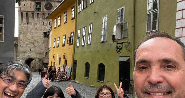 Des voyageurs souriants prennent un selfie dans une rue médiévale avec la tour de l'horloge jaune de Sighișoara et des maisons colorées en arrière-plan
