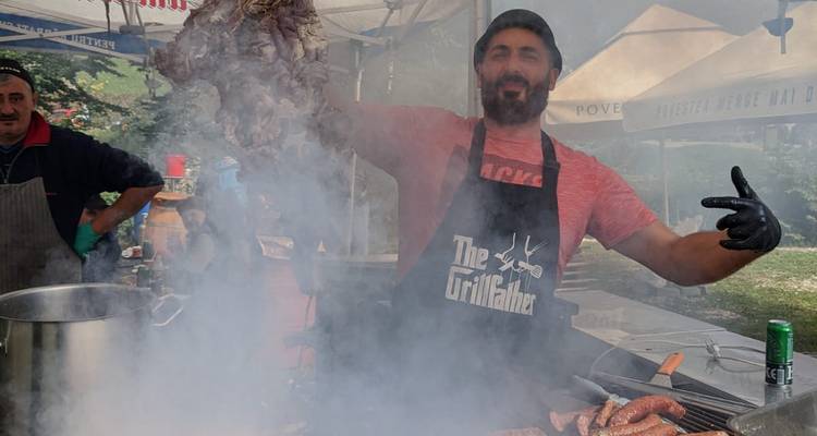Vendeur de street-food soulève de la viande grillée à travers la fumée tourbillonnante à un stand de grill en plein air