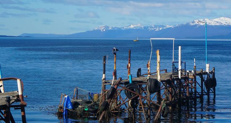 Ein rustikaler Steg, der sich in ein ruhiges Gewässer erstreckt, mit Bergen im Hintergrund.