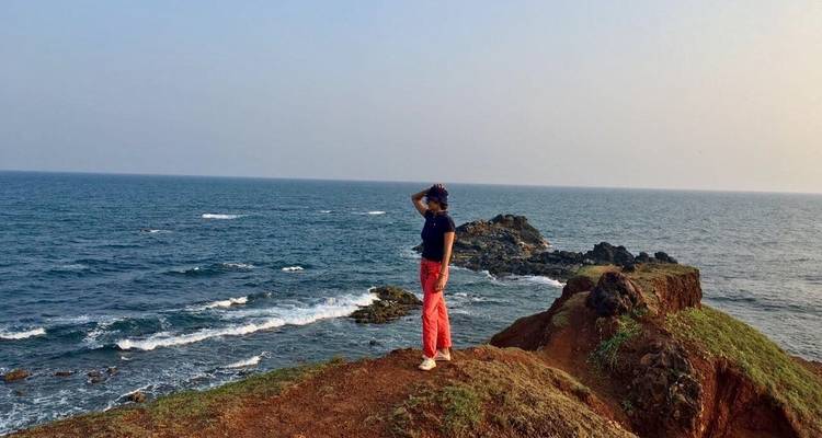 Person, die auf einer Klippe steht und auf das Meer mit brechenden Wellen blickt.