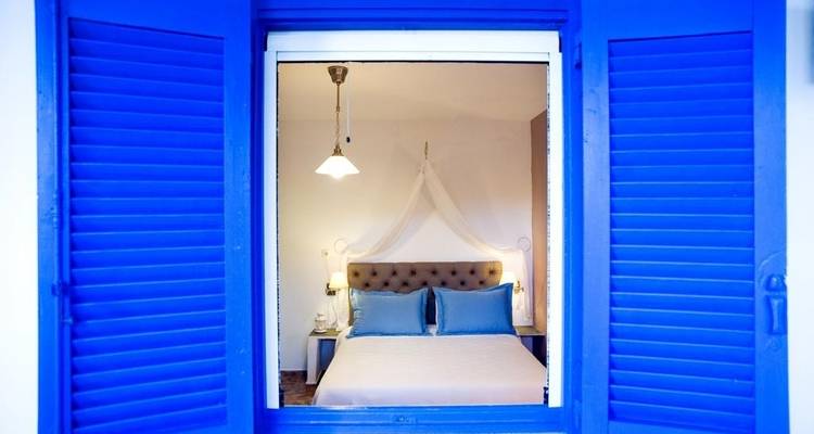 Chambre à coucher avec volets bleus et lit à baldaquin en Grèce.