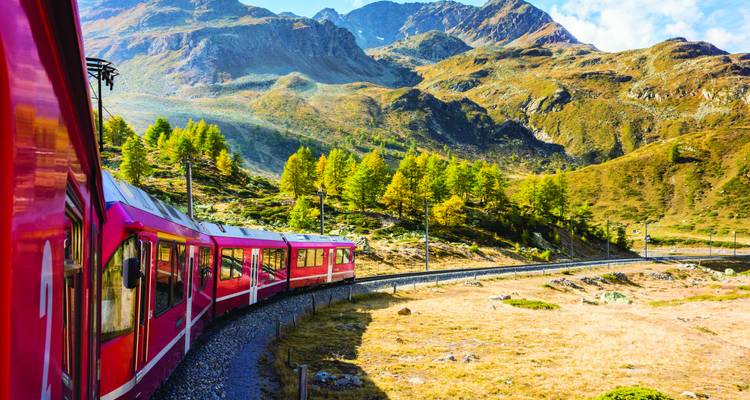Le train rouge vif Bernina Express serpente à travers des forêts de mélèzes dorés et des paysages alpins rocheux.