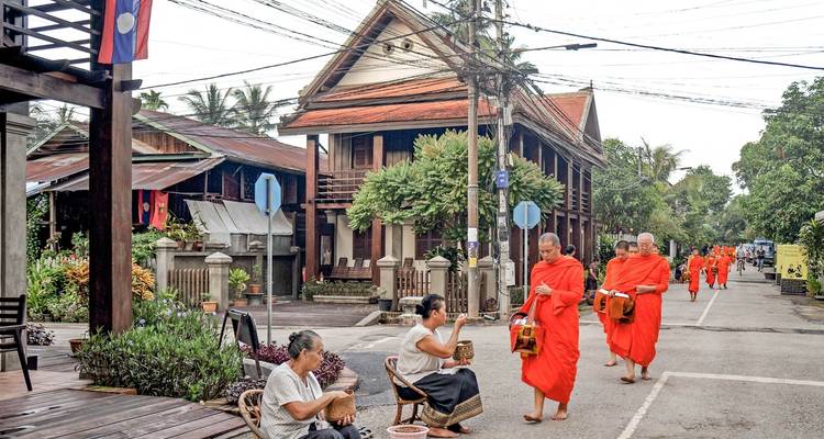 Monks and locals in traditional attire on a quiet street, with a Lao flag visible.
