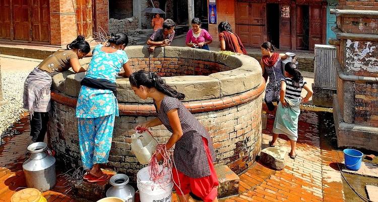 Local women drawing water from a communal well in a village setting.
