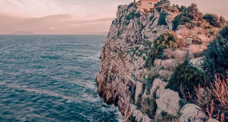 Vue panoramique d'une maison perchée sur une falaise rocheuse au-dessus de l'océan.