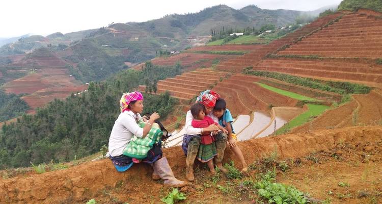 Personas en vestimenta tradicional descansando en una ladera con vista a terrazas de arroz.