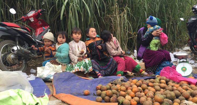 Niños sentados en el suelo junto a frutas para la venta.
