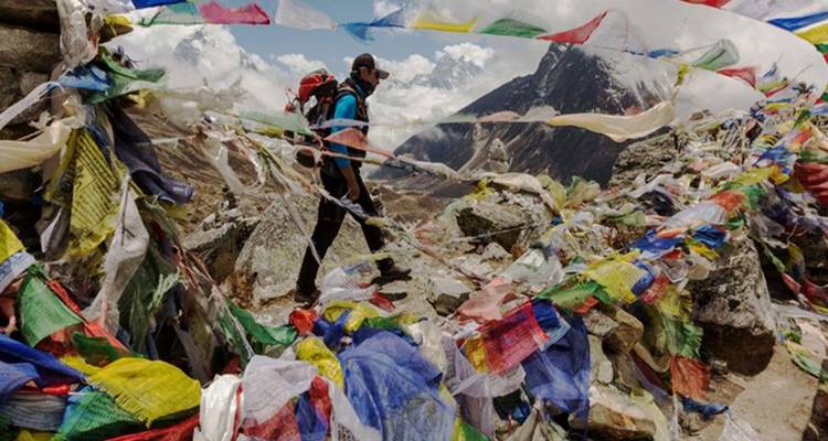 Wanderer geht durch tibetische Gebetsfahnen mit Berggipfeln im Hintergrund.