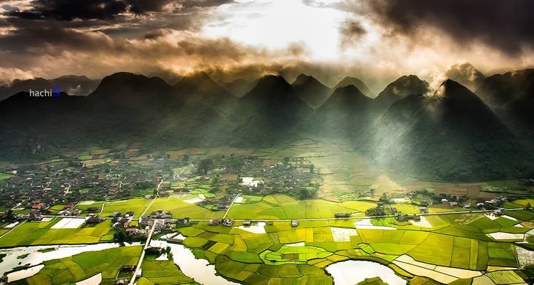 Sonnenstrahlen, die durch Wolken über eine bergige Landschaft mit Feldern dringen.