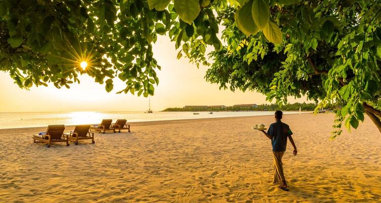 Een persoon die bij zonsondergang over het strand wandelt met ligstoelen.