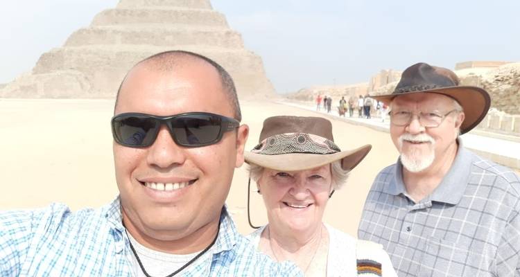 Deux touristes prenant un selfie avec une pyramide égyptienne en arrière-plan.