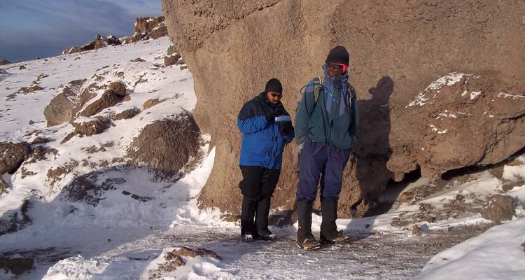 Dos excursionistas descansando contra una roca grande en condiciones nevadas.