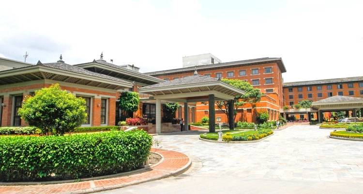 Bâtiment d'hôtel avec une cour verte sous un ciel nuageux.