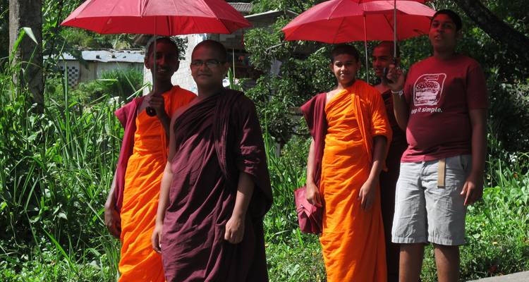 Groupe de moines et un homme marchant sur un sentier tenant des parapluies rouges.