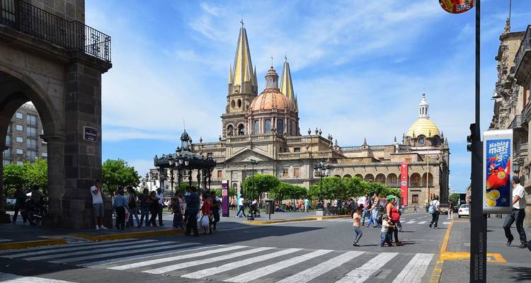 Una plaza de la ciudad concurrida con una catedral y gente cruzando la calle.