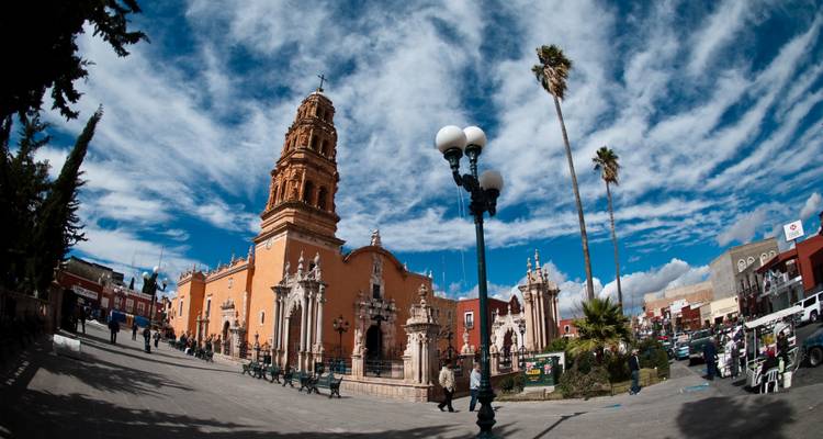 Un paisaje urbano con una torre de iglesia alta y gente alrededor.