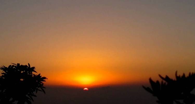 Sonnenuntergang über einer Landschaft mit Silhouetten von Bäumen.