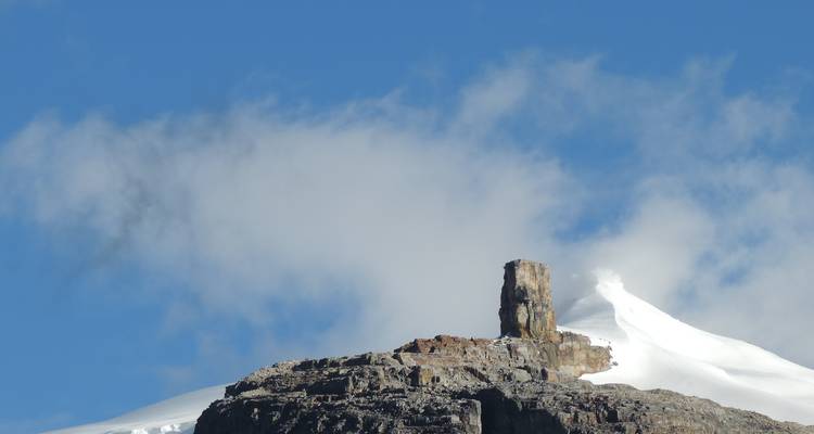 Pico de montaña rocosa con cumbre nevada distante.