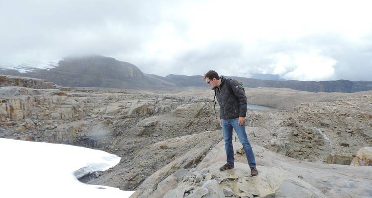 Persona explorando terreno rocoso con vista a un pico nevado.