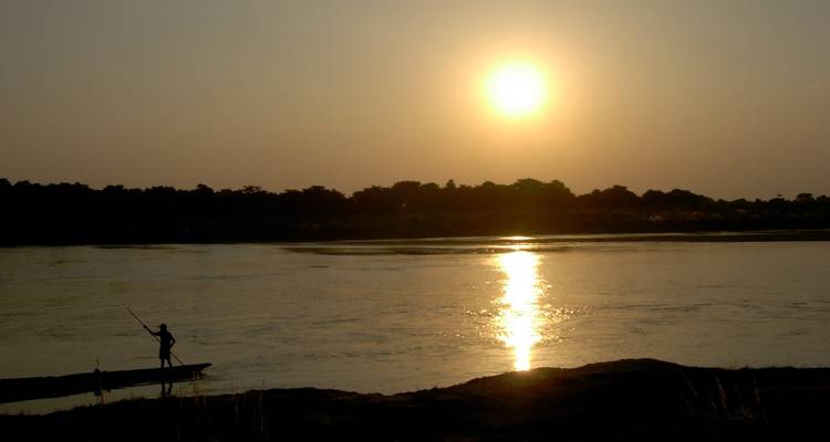 Silhouette d'une personne dans un bateau au coucher du soleil sur une rivière.
