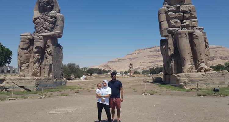 A couple with a child standing in front of the Colossi of Memnon.