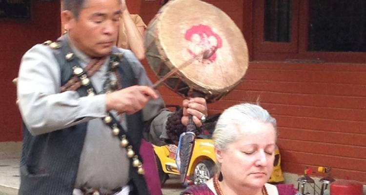 Ein Mann, der neben einer sitzenden Frau in traditioneller Umgebung Trommel spielt.